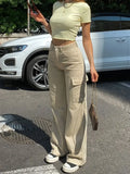 Frau in beiger Cargo-Hose und gelbem Crop-Top vor weißem Auto, modisch, urbaner Stil, Sommermode, lässiges Outfit, Sneakers, Handtasche.