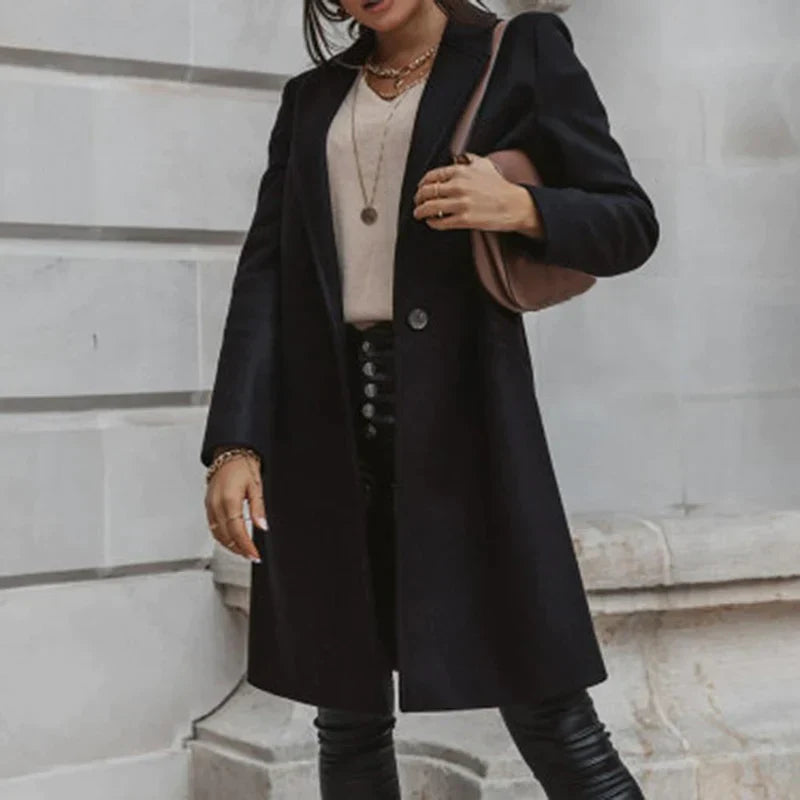 Frau in schwarzem Mantel und Lederhose vor grauer Wand, braune Tasche, modisches Outfit, Herbstmode, Streetstyle, elegante Damenbekleidung.
