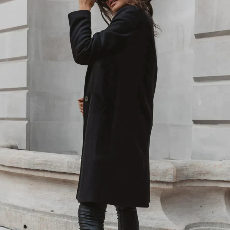 Frau in schwarzem Mantel vor urbaner Steinwand, modisch gekleidet, Herbstmode, eleganter Look, stilvolle Damenbekleidung, Stadtmode.