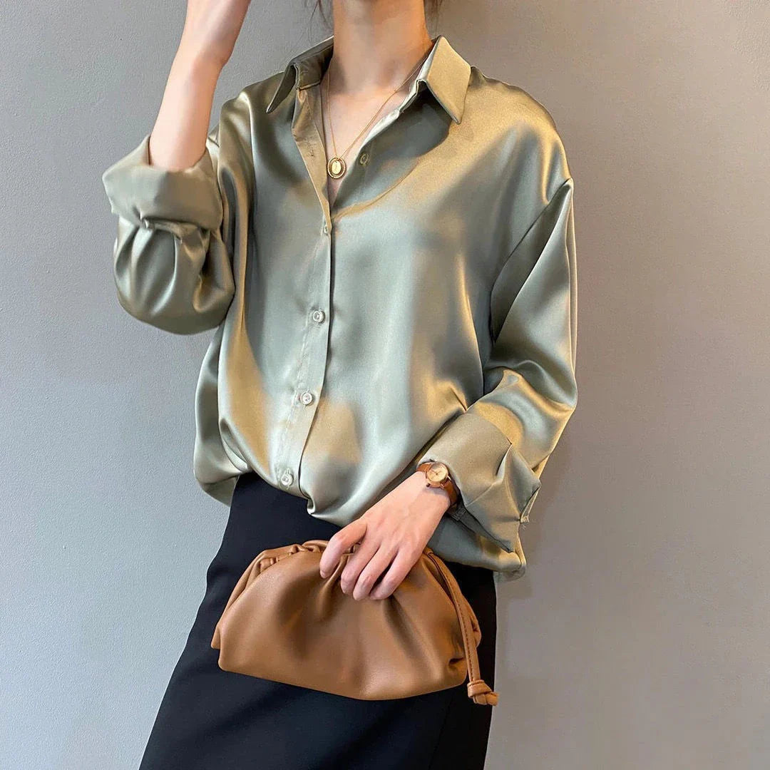 Frau in eleganter, glänzender Seidenbluse, hält braune Clutch. Modischer Look, ideal für Büro oder Abendveranstaltungen. Stilvolle Damenmode.