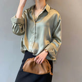 Frau in eleganter, glänzender Seidenbluse, hält braune Clutch. Modischer Look, ideal für Büro oder Abendveranstaltungen. Stilvolle Damenmode.