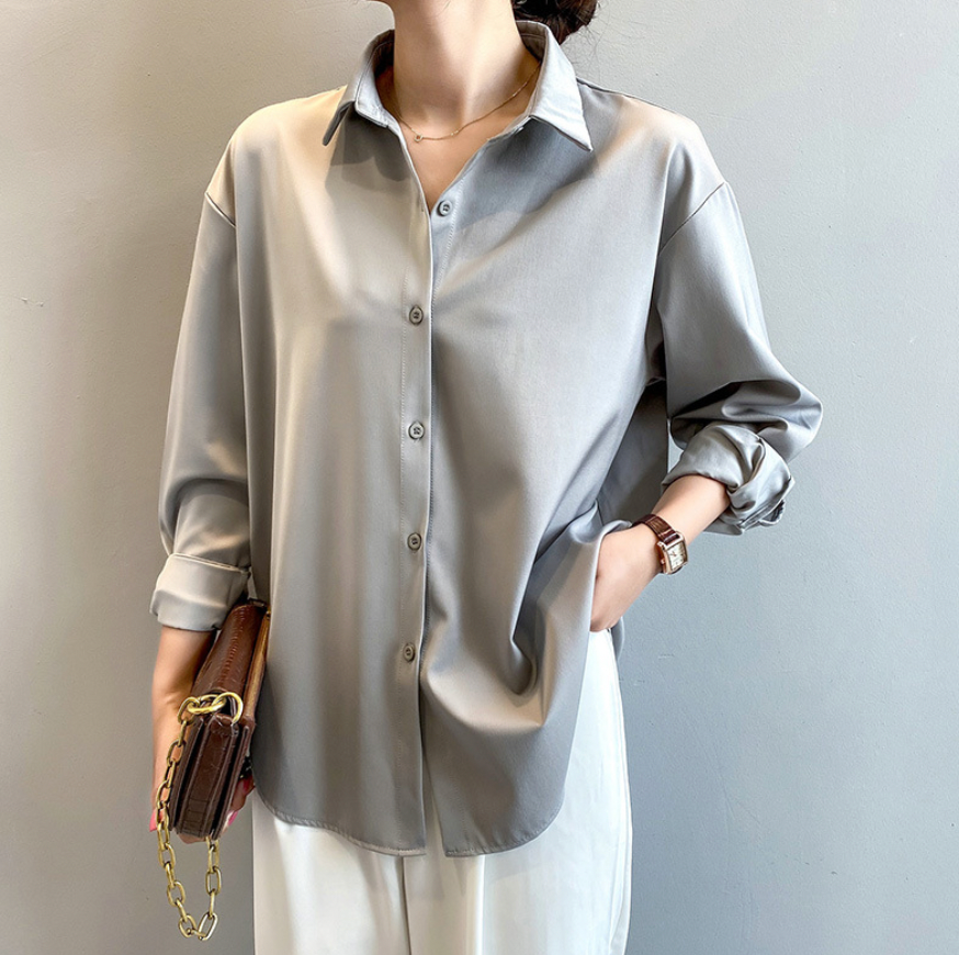 Elegante Frau in grauer Bluse und weißer Hose, hält braune Handtasche. Modetrend, Damenmode, stilvolle Kleidung, Freizeitlook.