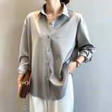 Elegante Frau in grauer Bluse und weißer Hose, hält braune Handtasche. Modetrend, Damenmode, stilvolle Kleidung, Freizeitlook.