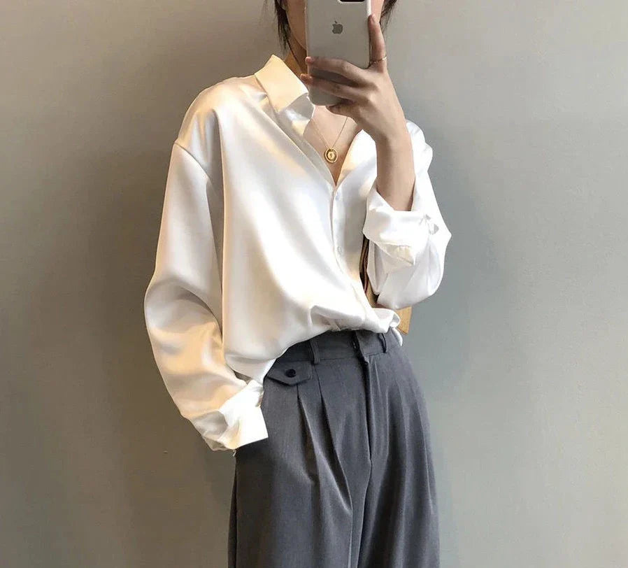 Frau in weißer Bluse und grauer Hose, hält Smartphone. Elegante Mode, minimalistisch, Business-Look, moderne Kleidung, stilvoller Auftritt.