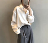 Frau in weißer Bluse und grauer Hose, hält Smartphone. Elegante Mode, minimalistisch, Business-Look, moderne Kleidung, stilvoller Auftritt.