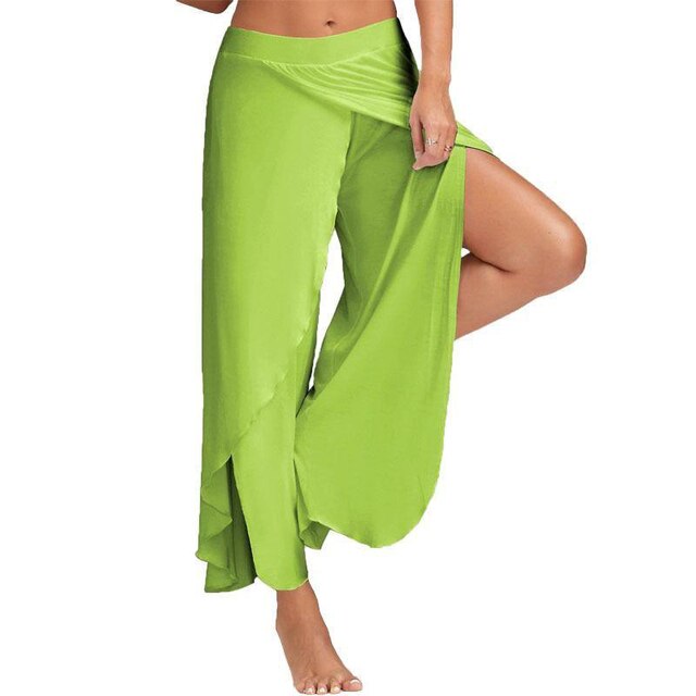 Frau in grüner, fließender Haremshose, zeigt Bein. Modetrend, bequeme Sommerkleidung, lässiger Stil, ideal für Yoga oder Strand.