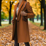 Frau im braunen Mantel im herbstlichen Park, umgeben von gelben Blättern. Herbstmode, stilvoller Mantel, Naturhintergrund, Spaziergang im Herbst.