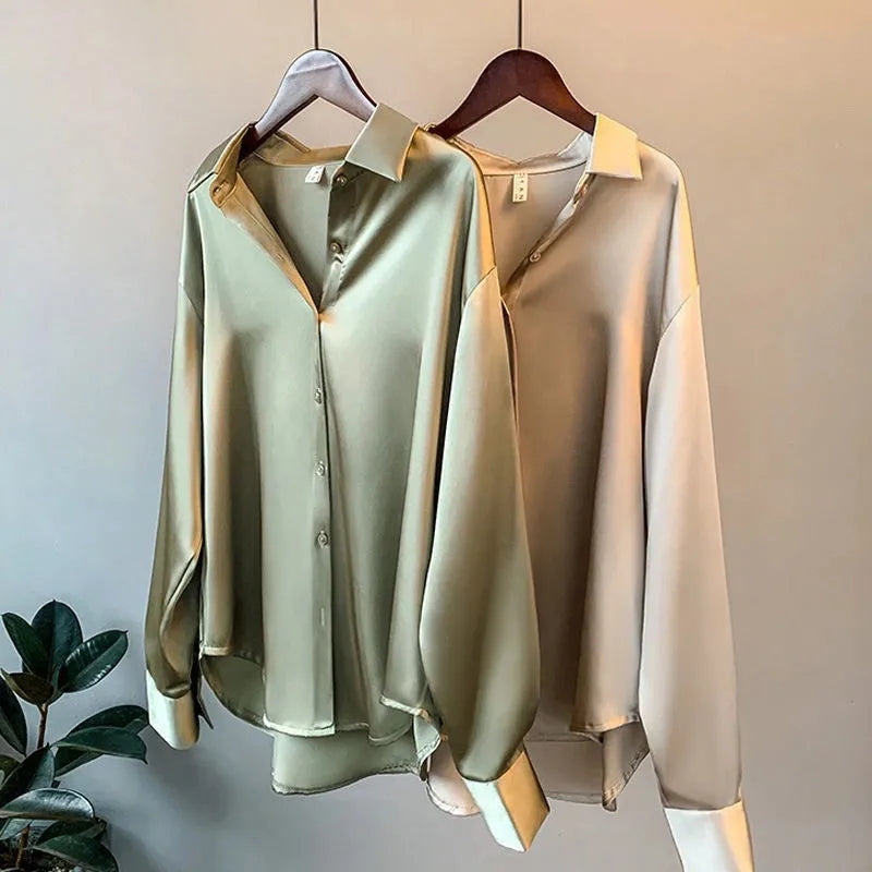 Zwei elegante Satinblusen in Grün und Beige auf Holzkleiderbügeln, minimalistisch, modisch, langärmlig, perfekt für Büro oder Freizeit.