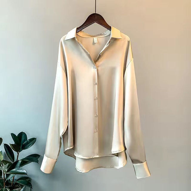 Elegante beige Seidenbluse auf einem Kleiderbügel, langärmlig mit Knopfleiste, vor grauem Hintergrund. Perfekt für Damenmode und Business-Outfits.